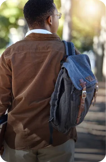 Student with a backpack walking outdoors on a tree-lined path