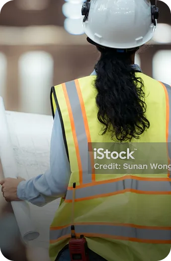 Construction worker in a yellow safety vest and white hard hat reviewing blueprints on a job site