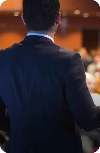 Man in a dark suit speaking to an audience at a corporate event