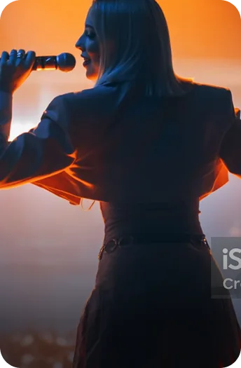 Female performer singing into a microphone on stage, lit by warm orange stage lighting