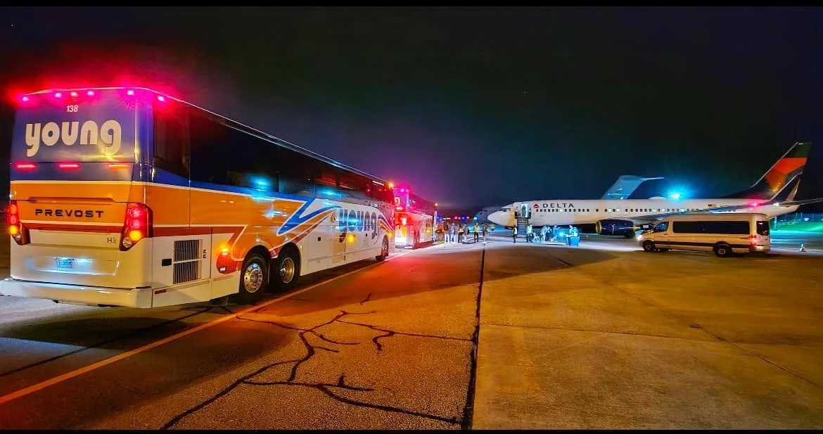 Young Transportation motorcoaches lined up on an airport tarmac at night beside a Delta Airlines aircraft