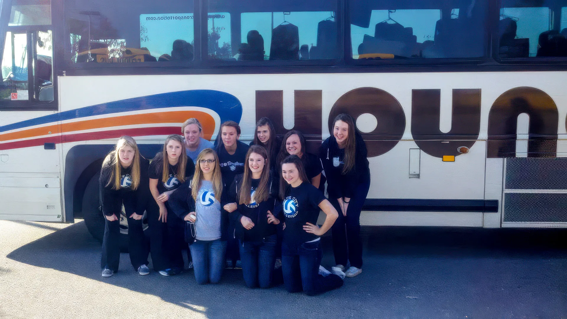 Girls volleyball team posing in front of a Young Transportation motorcoach before a charter trip