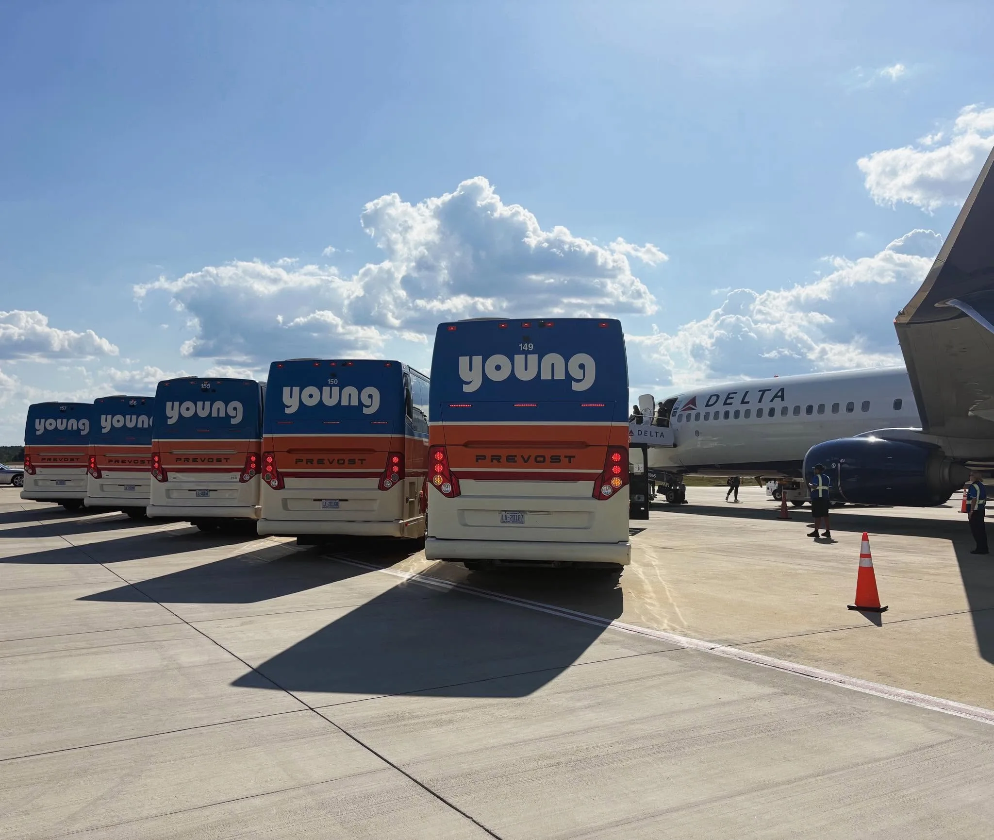 Five Young Transportation motorcoaches staged on an airport tarmac beside a Delta Airlines aircraft