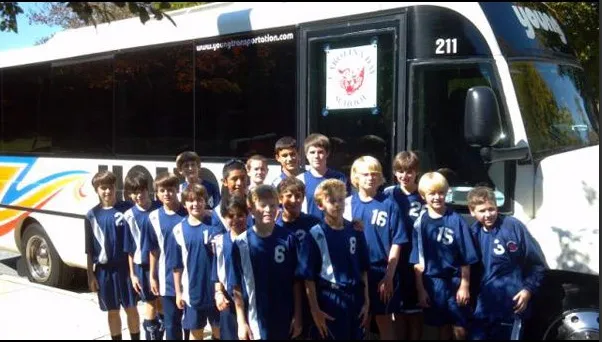 Youth soccer team in blue uniforms posing in front of a Young Transportation motorcoach